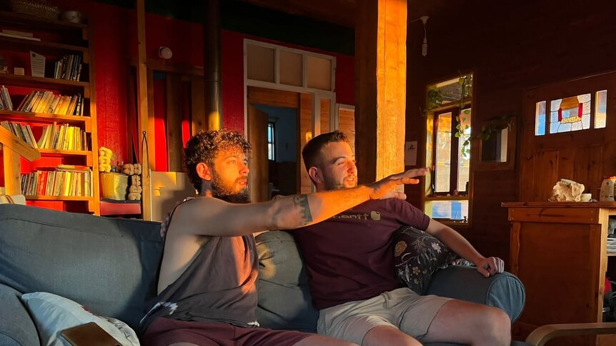 Two men sit on a couch as the sun shines on their faces