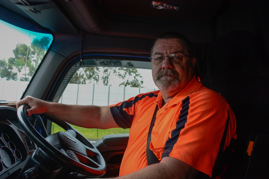 Man wearing orange hi-vis with his hand on the steering wheel sitting in a truck.