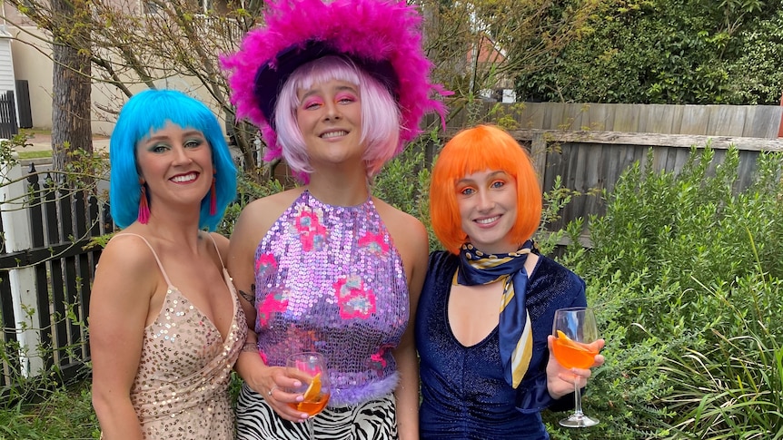 Amy and her housemates dressed in loud and glitter outfits with bright wigs, in story about lockdown birthdays..