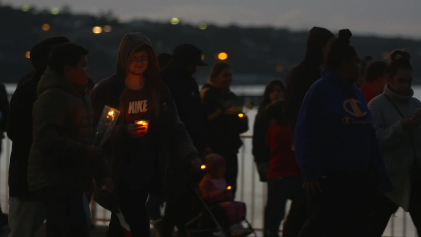 People walk at dusk holding candles