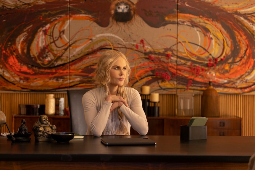 A woman sitting on a desk looking away.