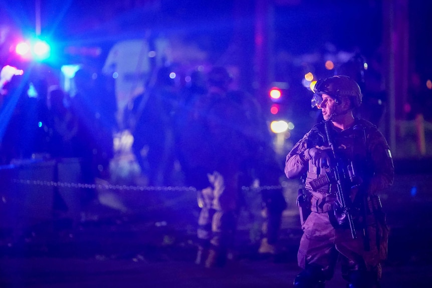 A National Guardsman holding a rifle standing in red and blue lights