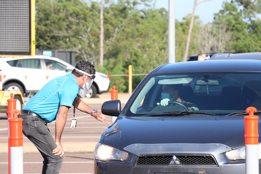 A man driving a car, wearing a face mask, speaks to a staff member at the COVID testing facility in Marrara.