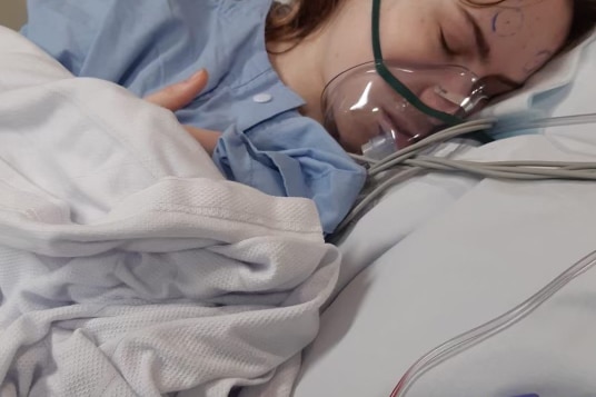 A girl lies in a hospital bed with an oxygen mask on