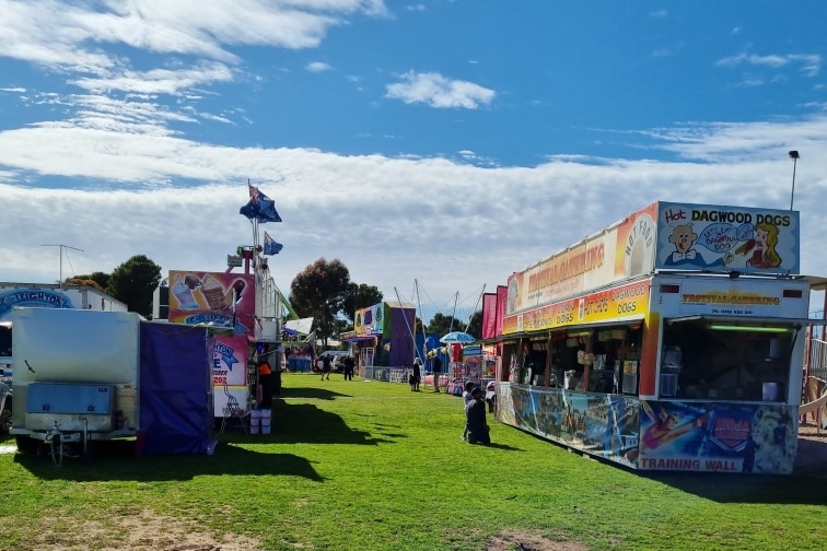 Line up of carnival attractions under a blue but cloudy sky