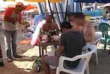 A dog-meat satay seller approaches tourists on a beach in Bali
