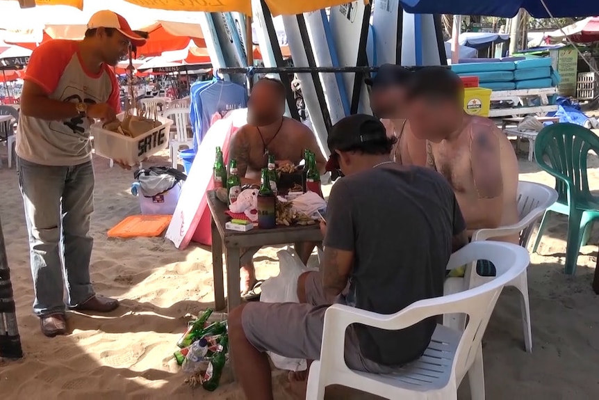 A dog-meat satay seller approaches tourists on a beach in Bali