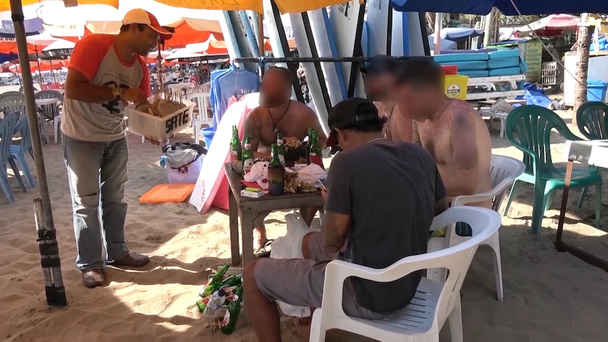A dog-meat satay seller approaches tourists on a beach in Bali
