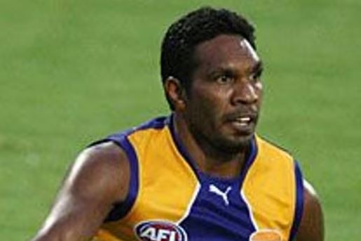 A man in a blue and yellow jersey kicks an AFL ball