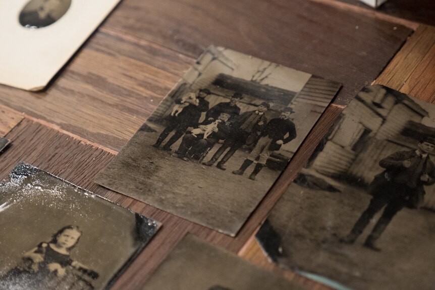 A tintype image of five men and two dogs on a wooden desk.