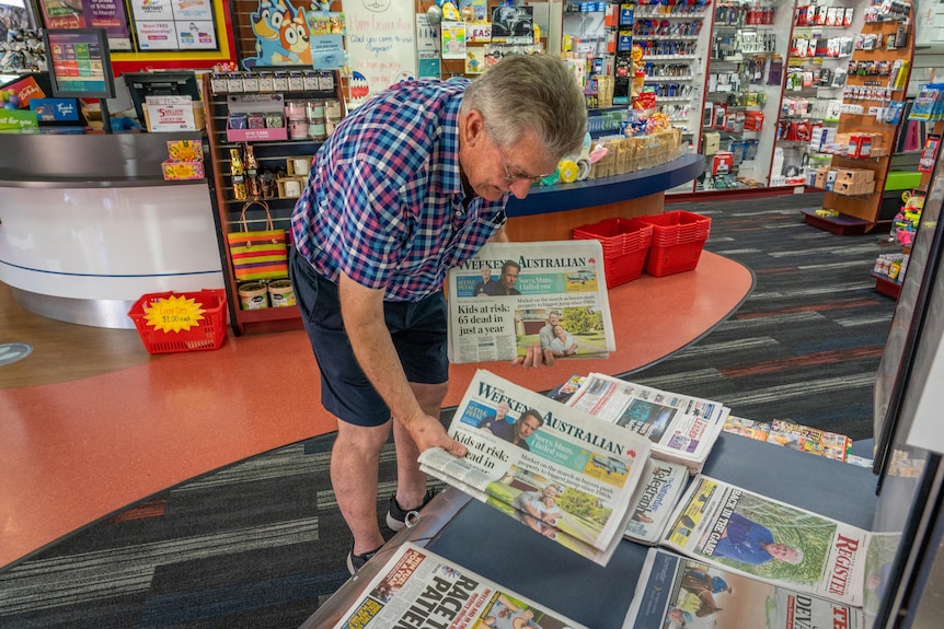 Un hombre coloca periódicos en una pantalla en un quiosco.