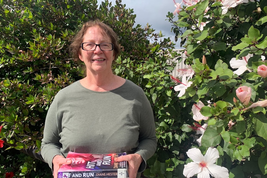 Author Diane Hester holding two of her books in front of a tree with white flowers.