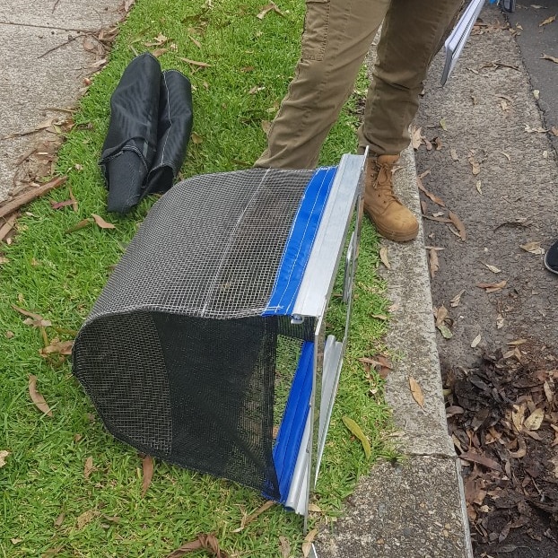 Un panier métallique sur l'herbe à côté d'un drain.