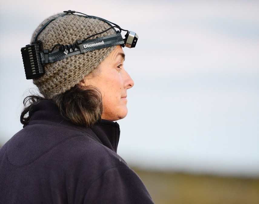 Uma mulher com chapéu e lanterna olha para longe. 