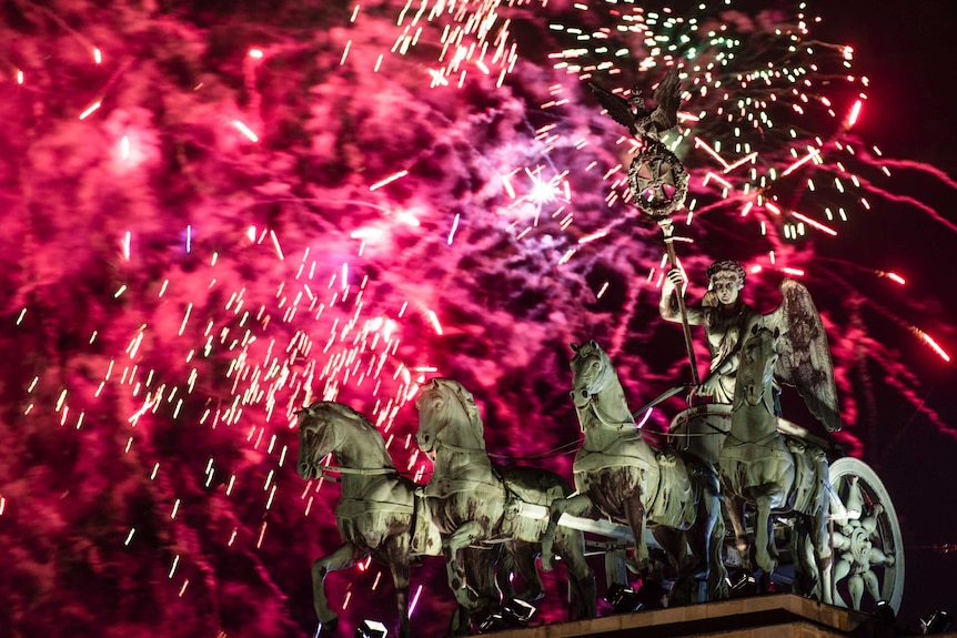 Pink and red fireworks light the sky above the Quadriga at the Brandenburg Gate.