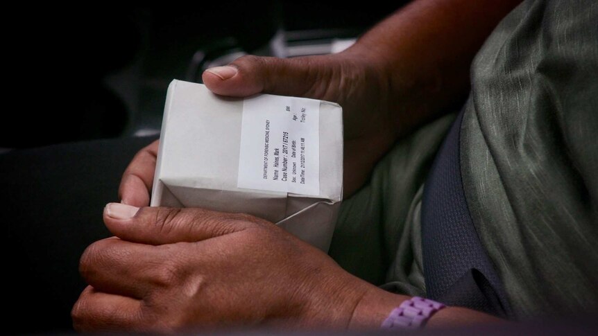 Two hands hold a small white package with a label on the front.