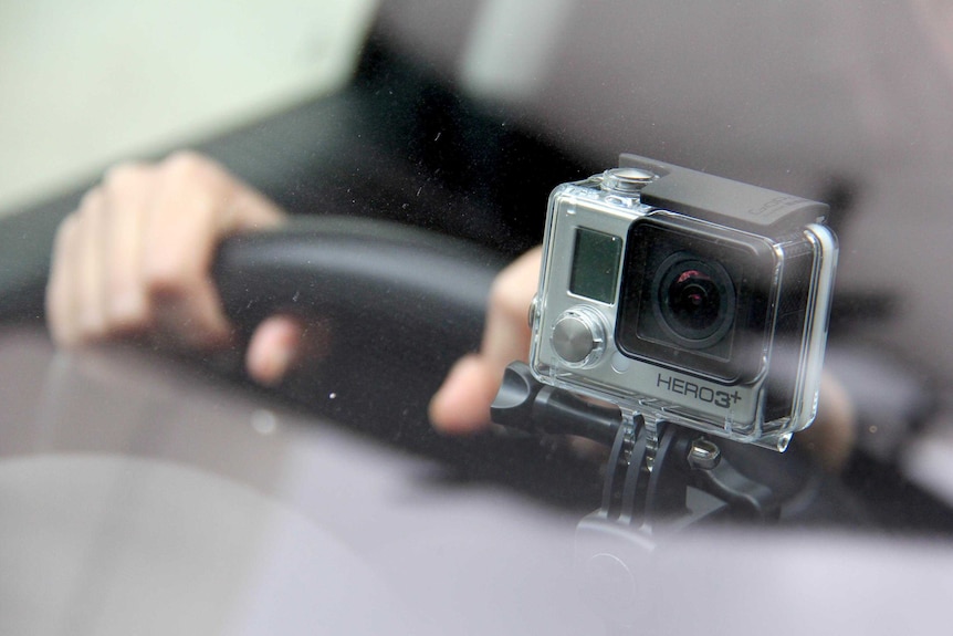 A dashboard camera is mounted near the windscreen in front of the steering wheel inside a car.