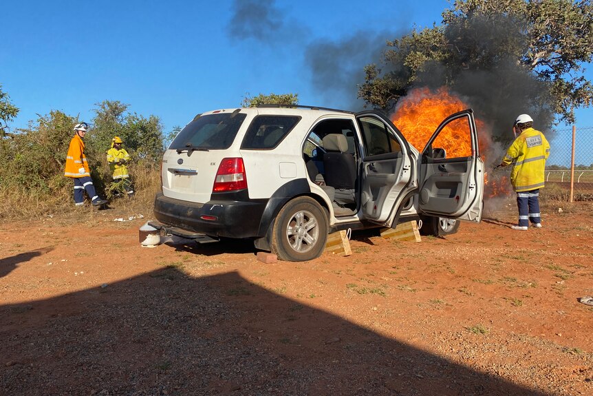 Firefighters stand back with hoses putting out a fire on the vehicle