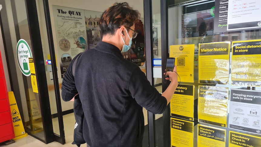 a man outside a supermarket using his iphone to register a qr code