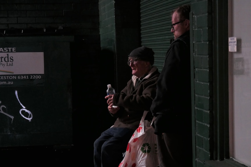 Two men next to a brick wall in the dark