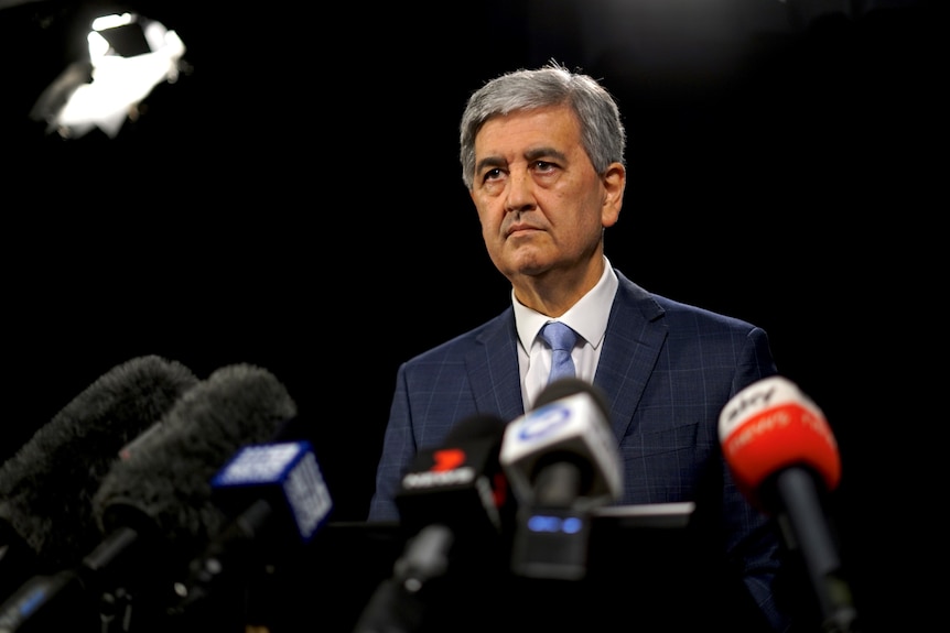 A man wearing a suit and tie looking grumpy with a black background