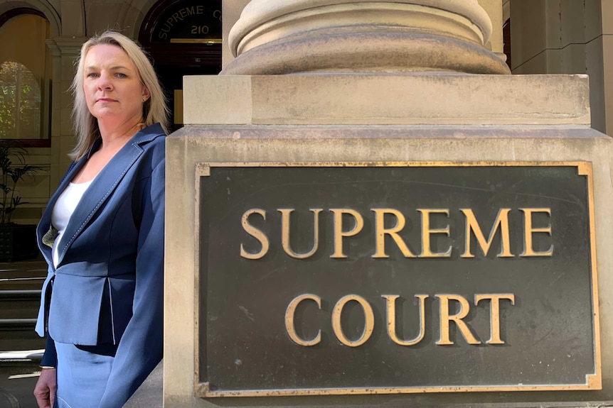 A woman with blond hair stands int he sunshine next to a pillar outside the Supreme Court.