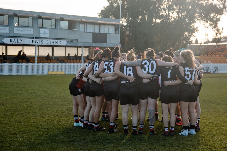 A women's football team bunch together in a huddle while on the field.