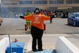 A photo of a female supervisor with her arms stretched out in front of two fancy cars.