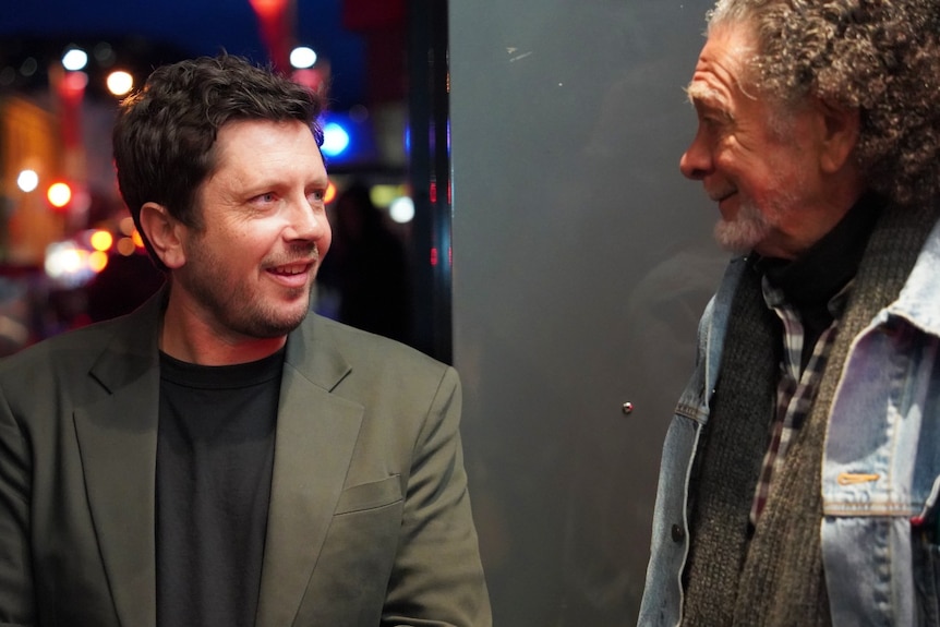 Two men stand outside a theatre and look at each other