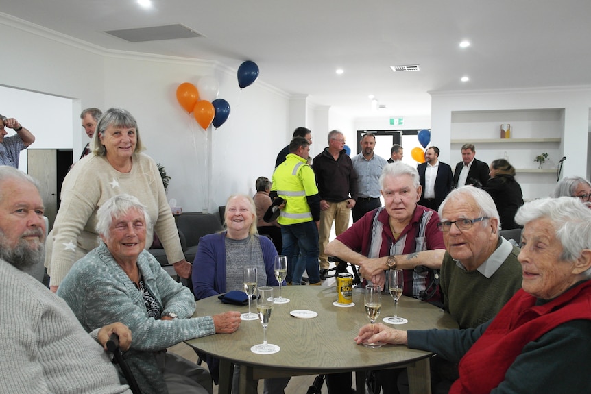 A group of retirees, drinking around a small table inside a room. 