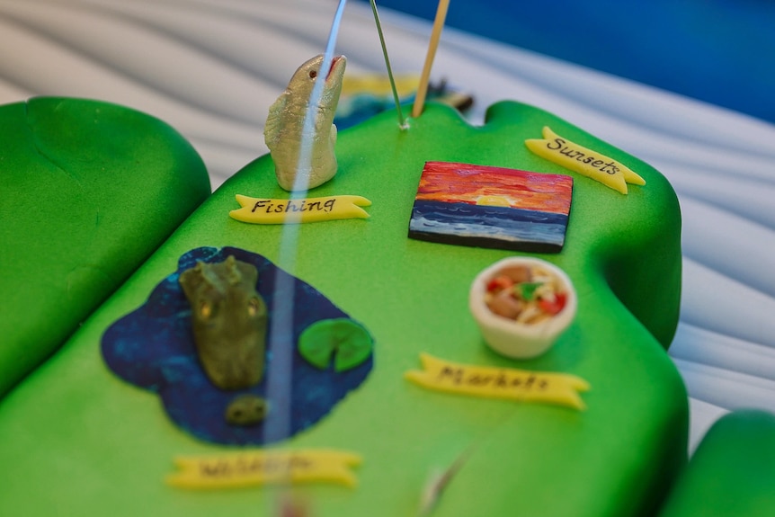 a crocodile, a barramundi, a jetski, a sunset, and a tiny bowl of laksa featured on a cake.