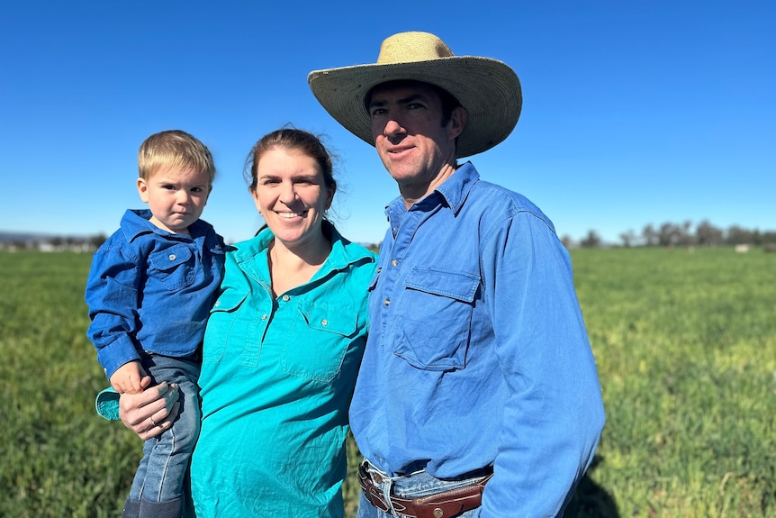 A man in hat stands beside a women in a green shirt, who is holding a toddler.