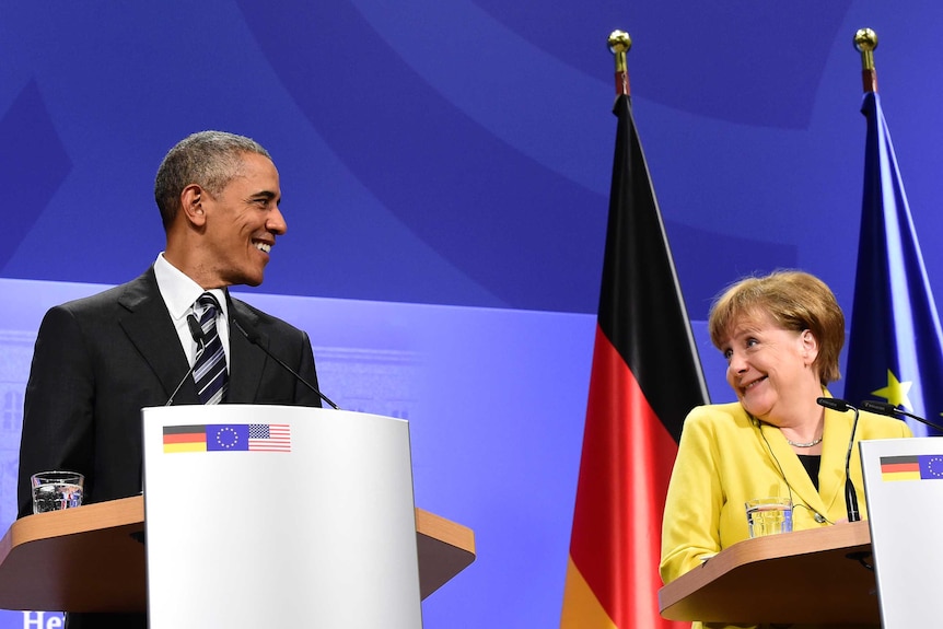 Barack Obama and Angela Merkel stand at lecterns to deliver a press conference.
