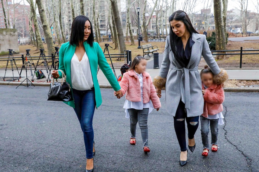 Two women walk outside a park with two little girls in matching pink fur jackets