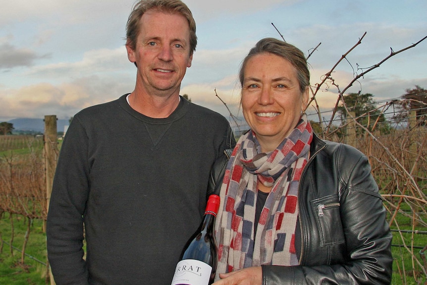 Man and woman standing in vineyard holding a bottle of wine.