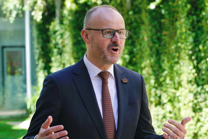 Andrew Barr wearing glases and a suit speaking.
