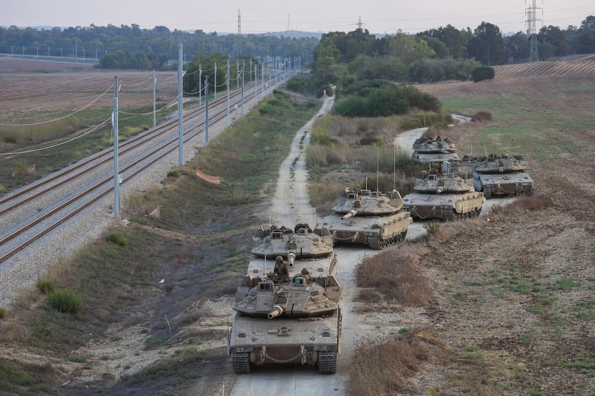 Israeli tanks move on a dirt road near a railway line near the Israeli Gaza border.