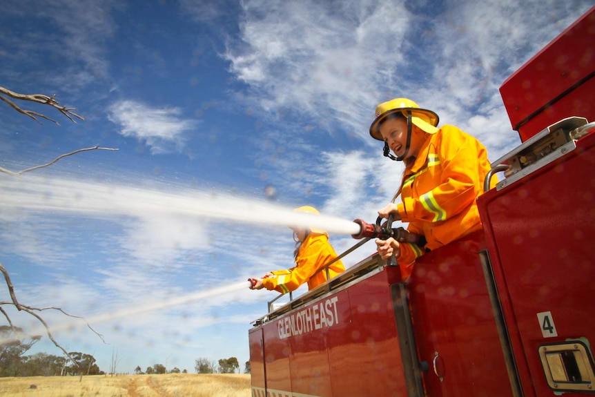 Two girls in yellow fire tunics spray hose from fire truck