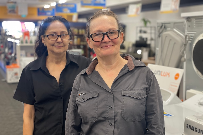 Two women standing in the middle of an electrical good store smiling 