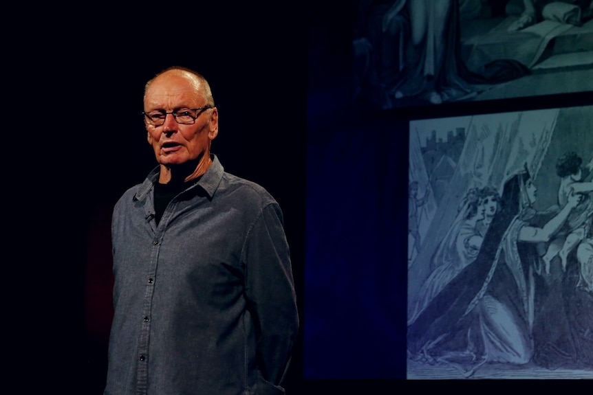 Older man on a stage in front of a historical drawing 