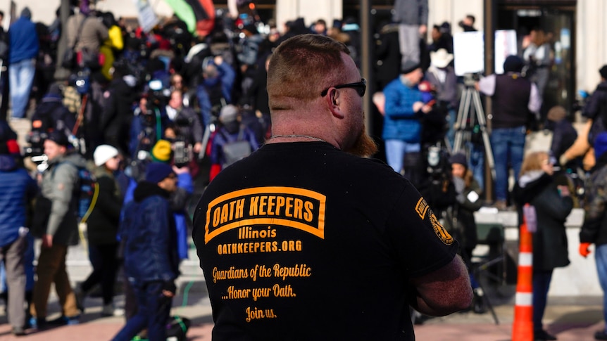 A man wearing an Oath Keepers shirt stands outside the Kenosha County Courthouse.