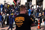A man wearing an Oath Keepers shirt stands outside the Kenosha County Courthouse.