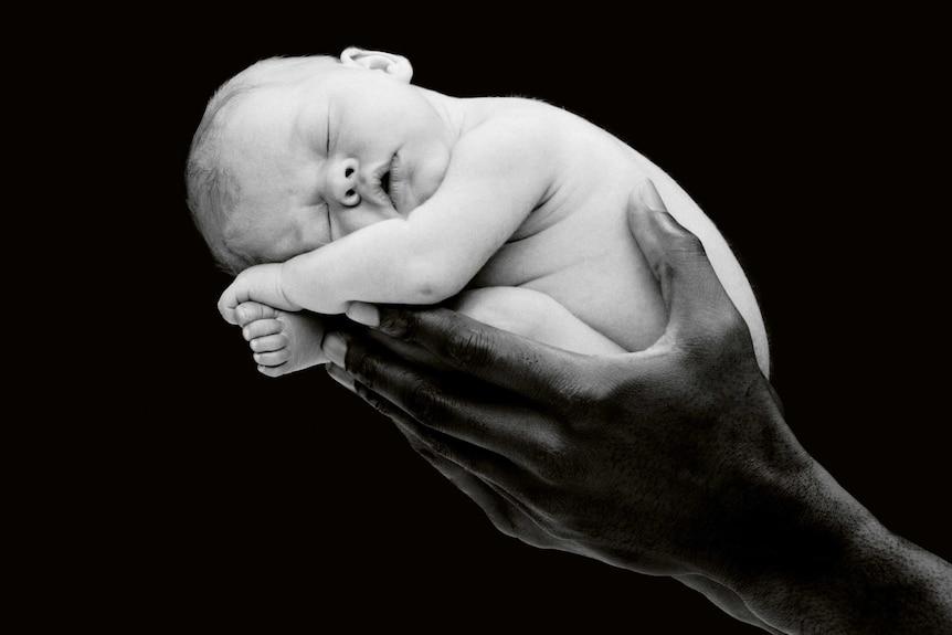 A black and white photograph by Anne Geddes, hands holding a small baby