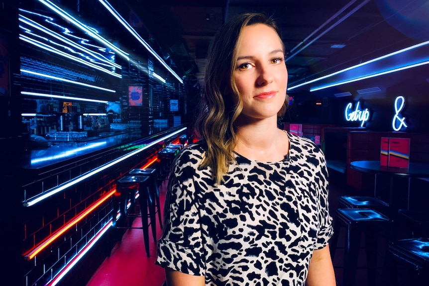 A woman stands in a room with neon lights behind her.