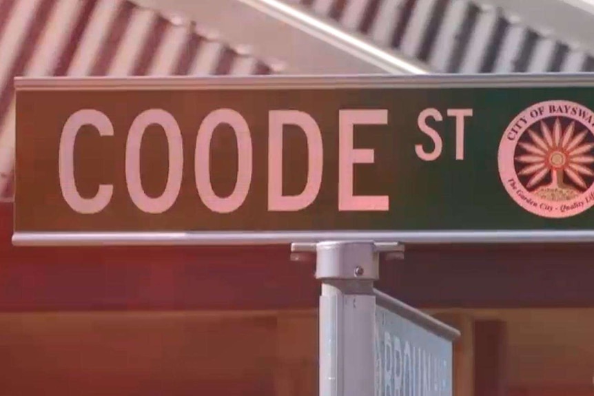 A street sign for Coode St with red police lights reflected on it.