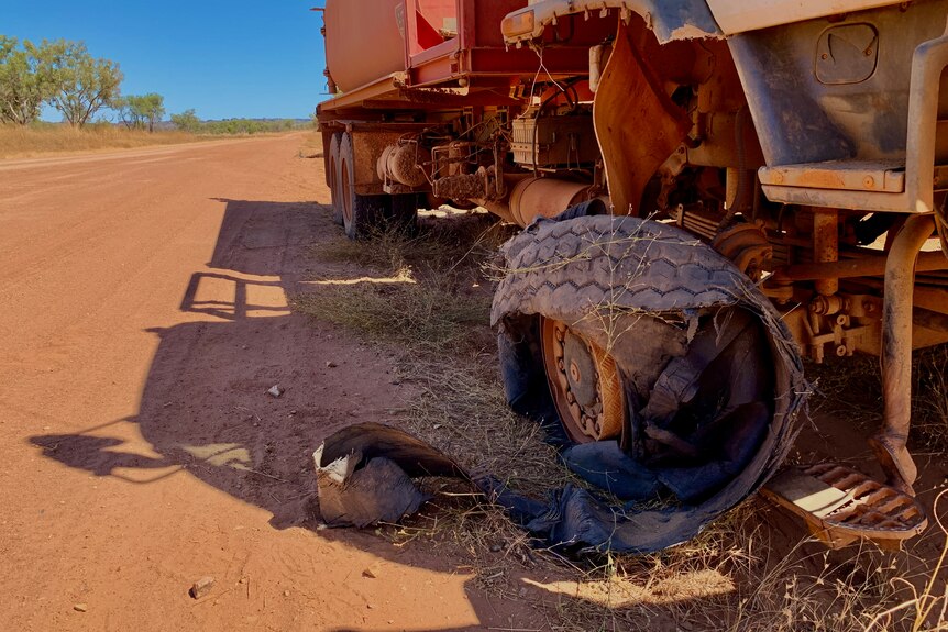 A shredded truck tyre sits on the edge of a rough dirt track.