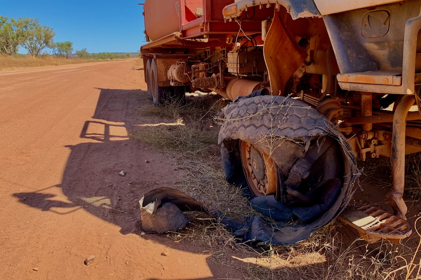 Un pneu de camion déchiqueté se trouve au bord d'un chemin de terre rugueux.