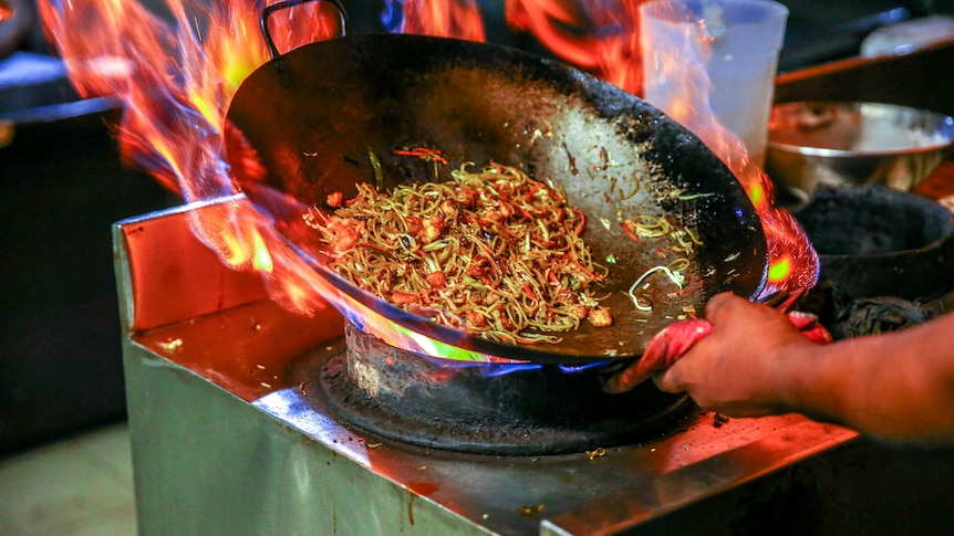 Noodles being tossed in a wok over a hot flame
