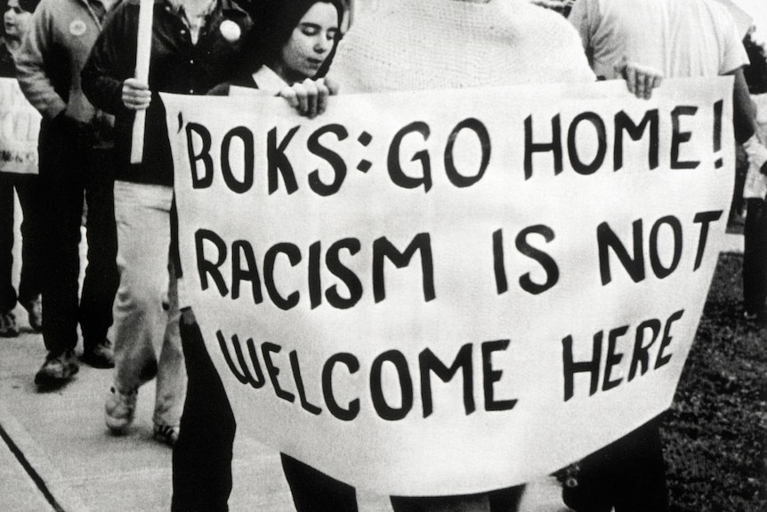 A woman holds a sign saying Boks go home! Racism is not welcome here