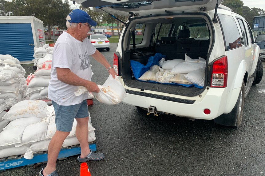 man loads sandbags into back of car.